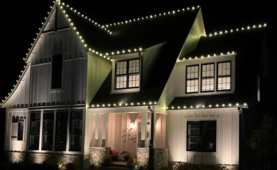 Modern farmhouse with white trim and steep gables lit along every edge after dark.