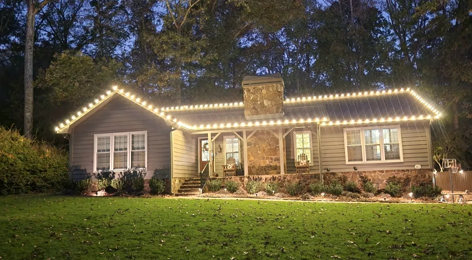 Long ranch-style house at dusk with one continuous roofline of lights over a green lawn.